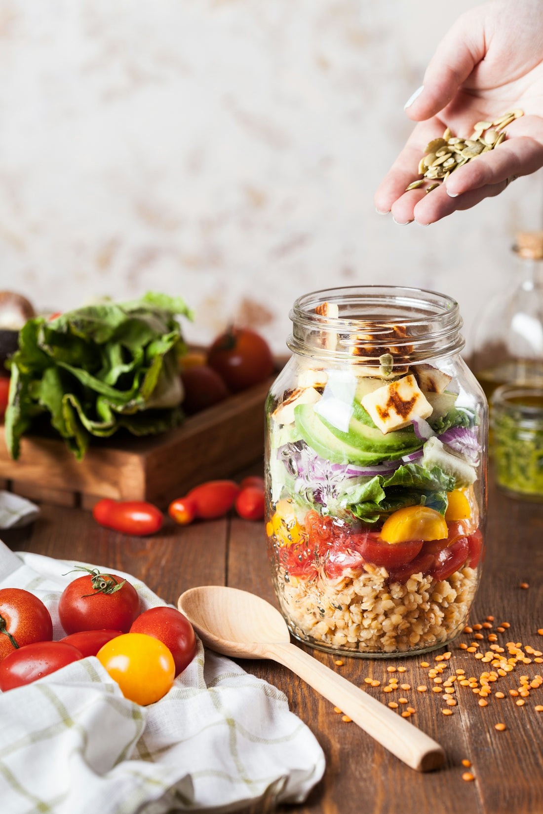 A hand sprinkling pumpkin seeds into a layered salad in a glass jar